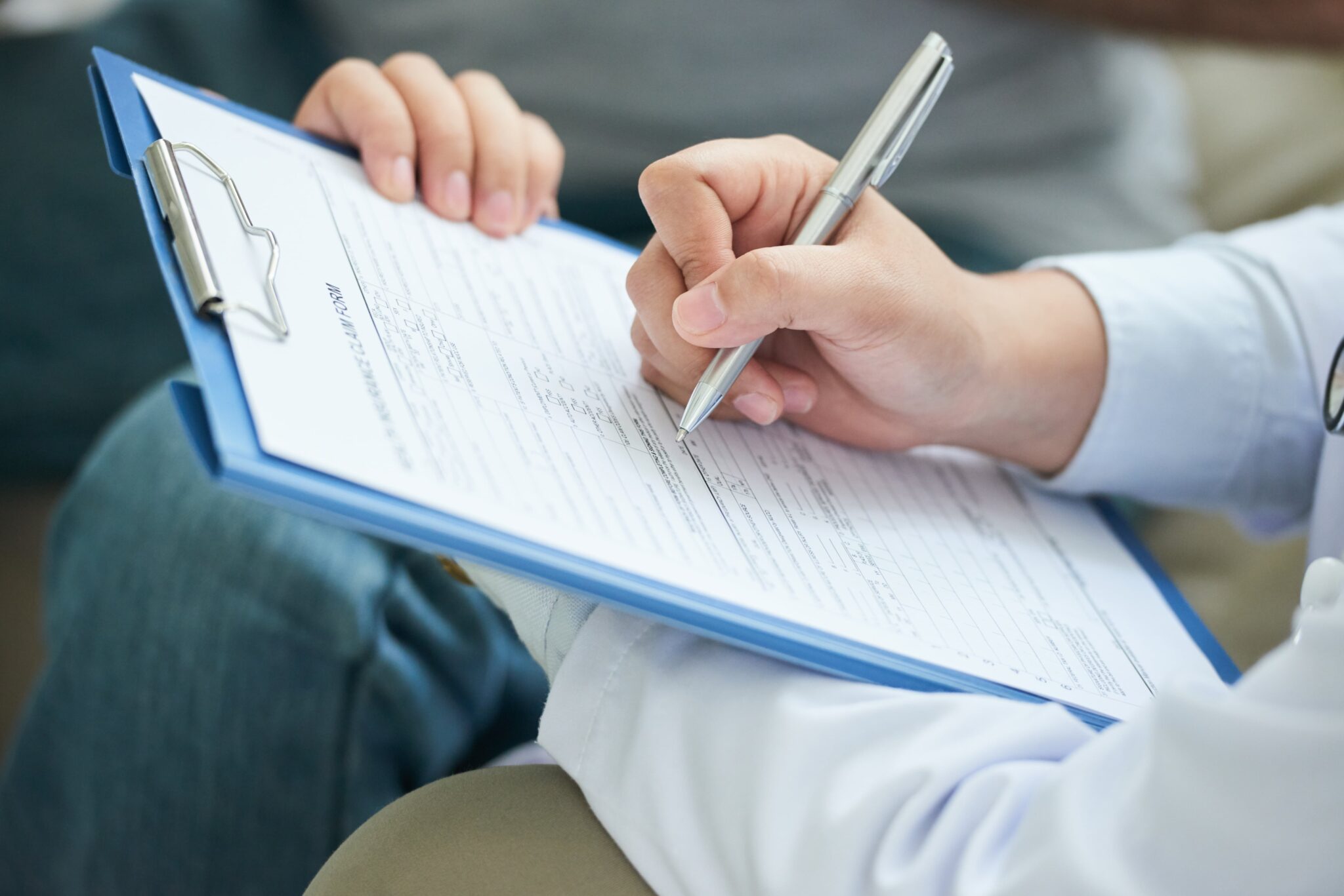 Person füllt ein Formular zur Patientenregistrierung beim Arztbesuch aus. Effiziente Gesundheitsverwaltung optimieren.
