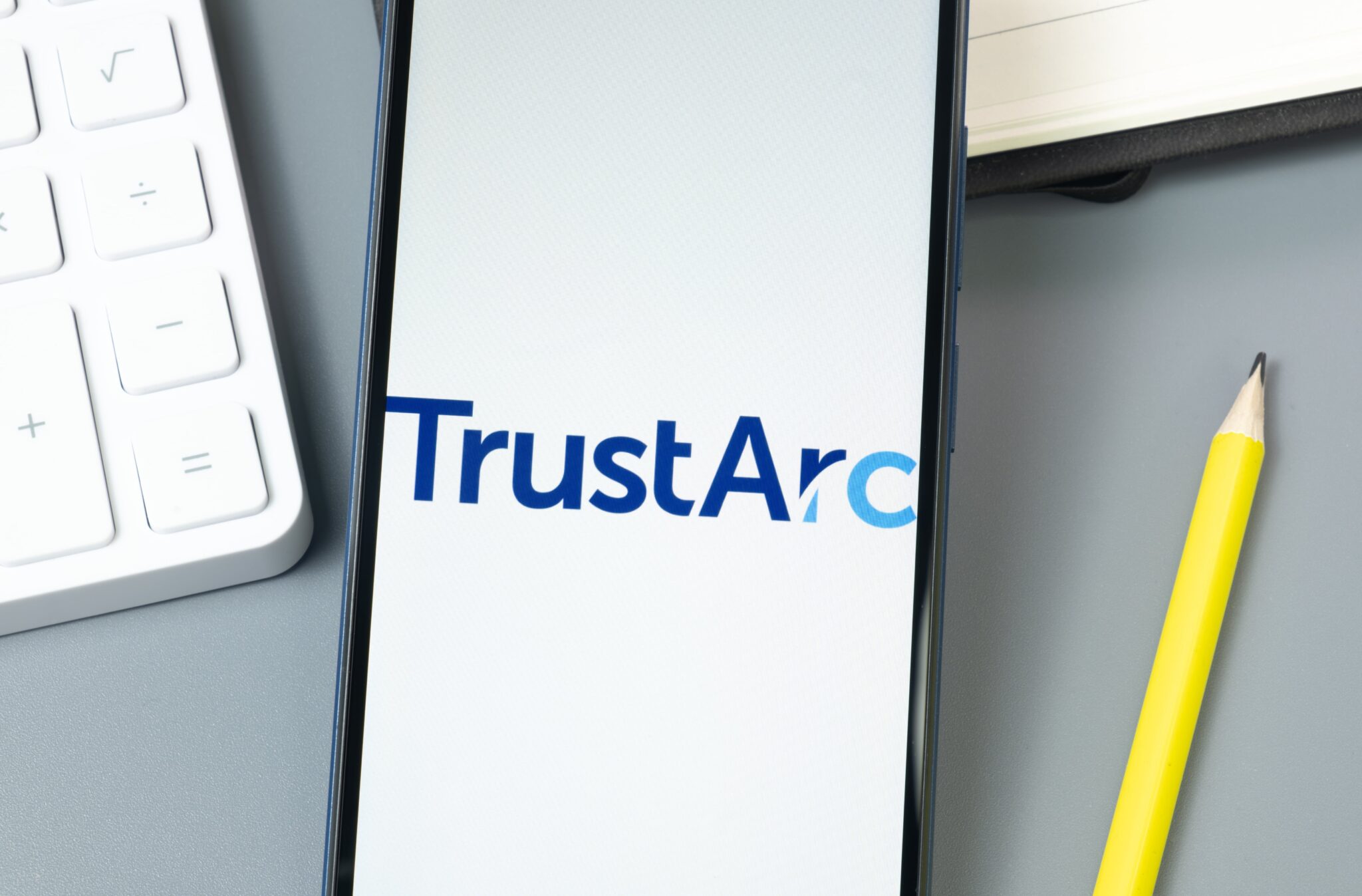 Smartphone mit TrustArc-Logo auf Schreibtisch, Fokus auf Datenschutzmanagement und Online-Sicherheit.